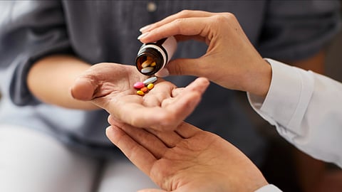 A person is giving tablets into one hand of a person from a small glass bottle.