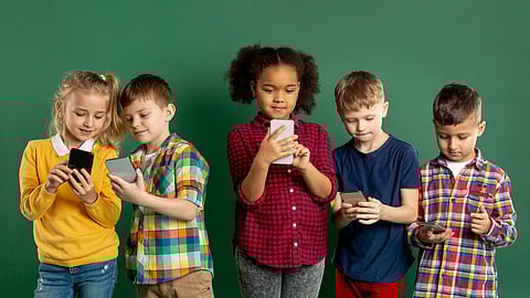 Image of children of different ethnicity using mobile phones in front of blackboard.
