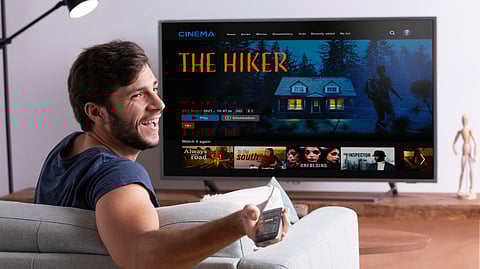 A man in a blue t-shirt is sitting on a sofa, binge-watching his favorite TV show.