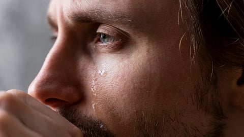 A close-up of a man crying and shedding tears.