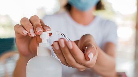 A girl in white shirt is pressing a bottle to dispense the hand sanitizer.