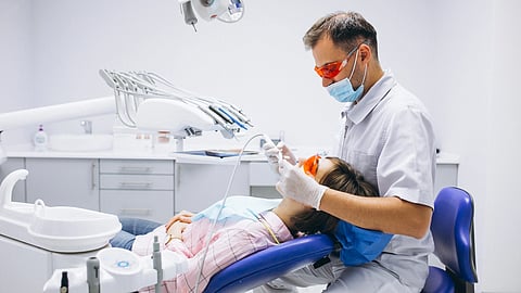 A woman patient lying on a dental chair and a male dentist doing a procedure.