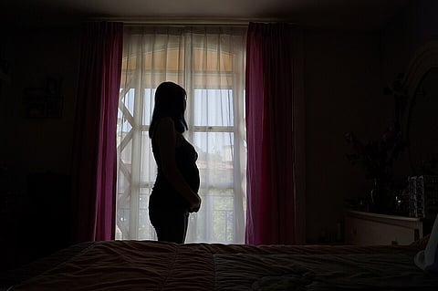 Pregnant women standing in the dark staring outside the window
