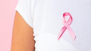 Woman wearing a white t-shirt having a pink bow made with ribbon representing breast cancer.