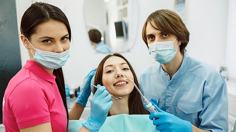A pair of dental students treating a patient in a dental chair.