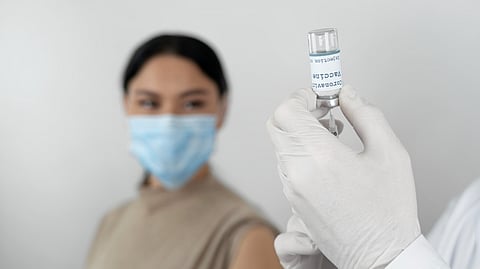 A woman is waiting for getting a vaccine shot and a person is getting the shot ready.