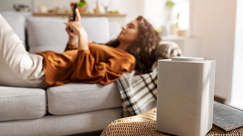 woman lying on bed wearing a brown top with an air cleaner on the side.