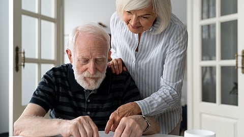 Image of a woman helping a man struggling with Alzheimer's disease in a household setting.
