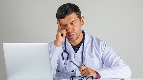 Image of a doctor in very depressing mode seeing his laptop.