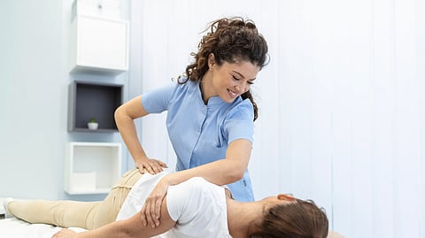 Young woman doctor physiotherapy or osteopath fixing lying womans back with hands movements during visit in manual therapy clinic professional chiropractor during work.