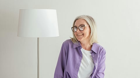 An image of an old woman wearing a lavender overshirt and smiling.
