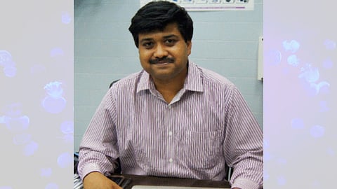 Image of Prof. Amit Singh wearing a purple striped shirt and sitting in front of blue background.