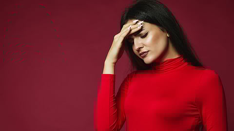 Image of a woman having long white nails wearing a red high-neck top in depressing mood.