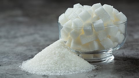 Image of sugar cubes in a transparent bowl and granulated sugar on floor.