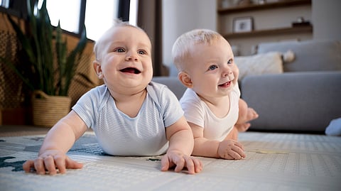 Image of two babies lying on a floor and smiling and playing together