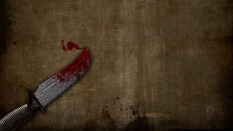 Image of a knife having blood stains all over it and around it in front of a woody background.