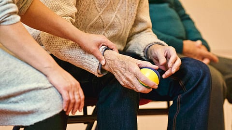 A caregiver supporting an elderly person holding a colorful ball during a wellness activity.