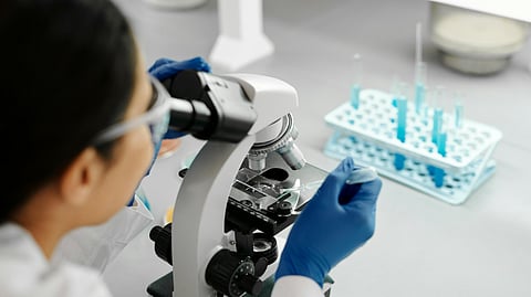 An image of a woman using a scientific device, a microscope, in a lab.