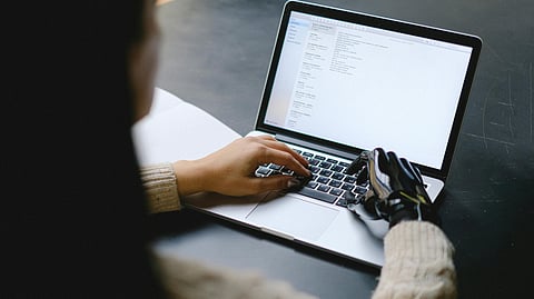 An image of a laptop and one human hand and one robotic hand on its keypad,.