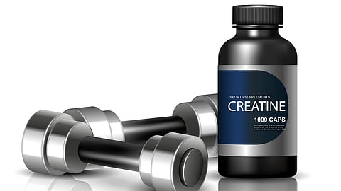  A sleek black bottle of creatine supplements labeled "1000 caps" sits beside a pair of silver dumbbells on a reflective white surface.