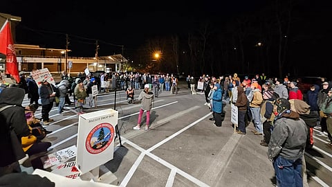 Nighttime protest with a crowd holding signs near a ballot drop box.