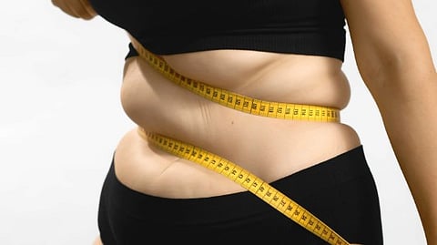 An obese woman winding a measuring tape around her tummy.
