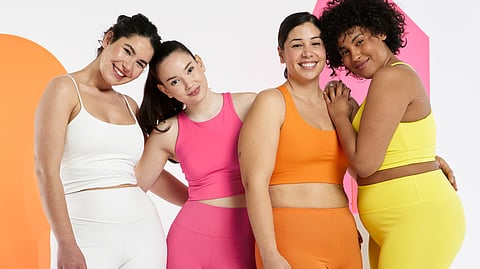 Group of four women in colorful activewear posing together and smiling.