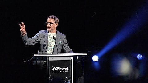 Robert Downey Jr. in a grey suit speaking on stage at a Disney event.