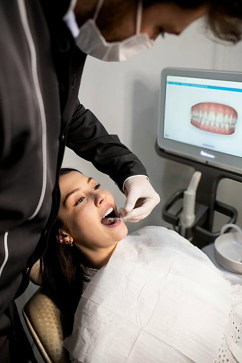 A woman undergoing a teeth cleaning procedure at a dental clinic, with a dentist working on her teeth.
