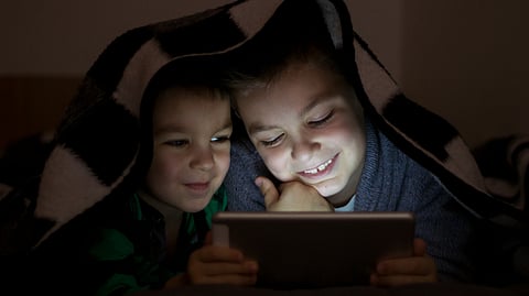 Image of 2 children watching phone at night.