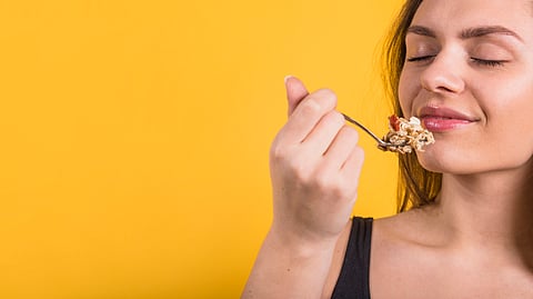 Woman eating food with a spoon against a yellow background.