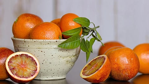 Image of oranges in a bowl and other oranges with a half-cut orange on the floor.