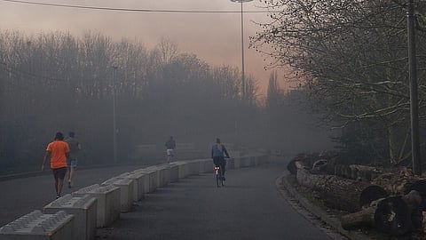 A polluted Delhi road with a man riding a bicycle while others walk, highlighting the city’s worsening air quality.