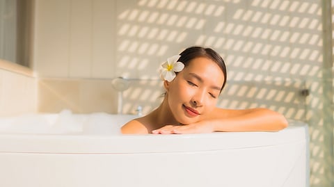 Image of a woman having a flower in her hairs and bathing in a bathtub.