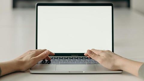 An image of a laptop with blank screen and two hands on the keyboard.