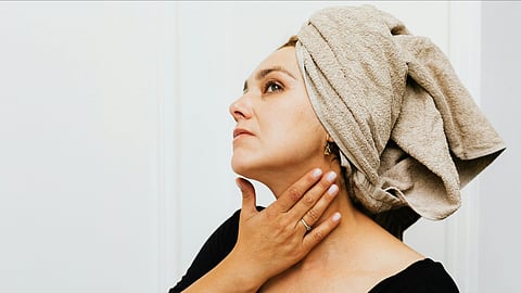 An image of a woman in a bath towel on head and touching her neck.