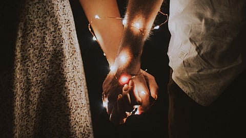 Image of hands of a couple together wrapped by lights.