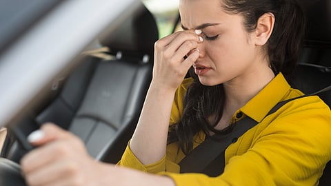 An image of a woman driving and having a headache.