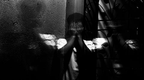An image of a boy sitting in a dark room, covering his face.