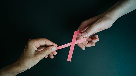 An image of a breast cancer awareness pink ribbon between 2 hands.