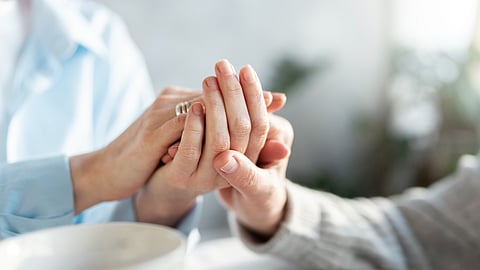 Close-up image of caregiver holding hands of an elderly Parkinson’s patient.