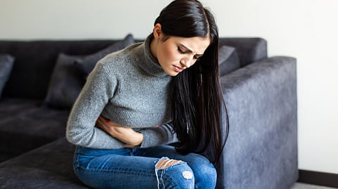 A woman is clutching her stomach due to pain and sitting on a sofa in the living room.