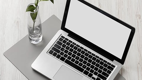 Image of a laptop with a flower in a vase on the table.