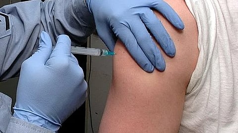 A nurse administering a vaccine to a person’s arm, wearing blue gloves.