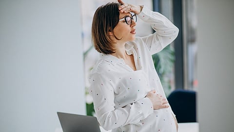 A young pregnant lady wearing white pyjama set looking stressed.