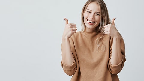 Image of a woman wearing brown cardigan, smiling and giving thumbs-up.