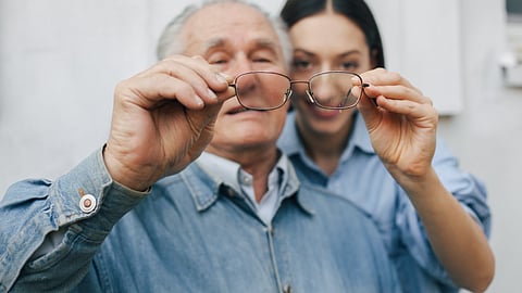 Image of an old man and woman in blurred background seeing through the glasses.