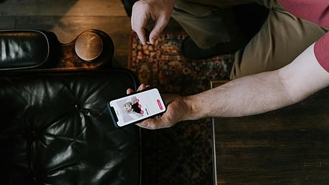 An image of a person sitting with a phone with a dating app on screen.