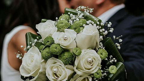 Image of a white bouquet in front of a blurred background having groom and bride.