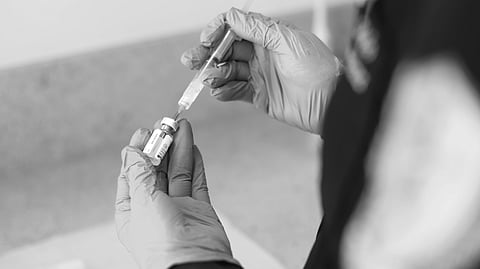 Black and white image of a nurse wearing gloves, drawing a vaccine from a vial.